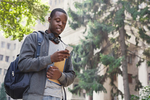 black male student looks at his phone while carrying his backpack