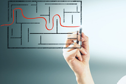 Hand drawing a red line through a maze from one side to the other.