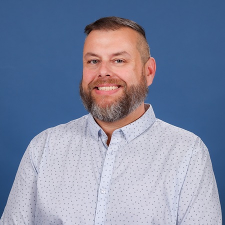 Smiling man with a trimmed beard in a studio portrait against a blue background
