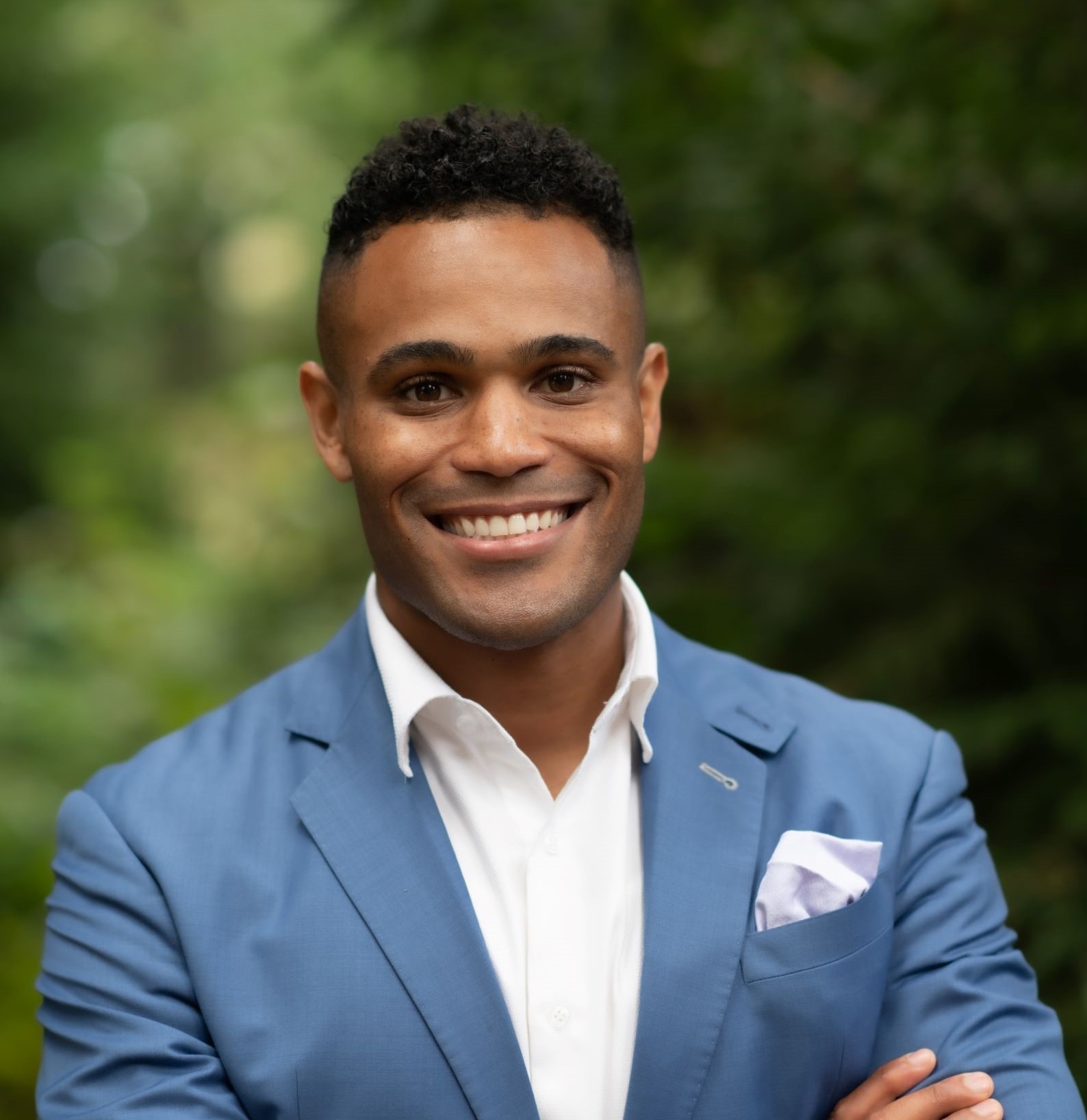 Smiling man in a blue suit jacket and white shirt against a blurred green background