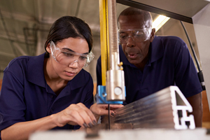 student works on a table saw as a teacher supervises