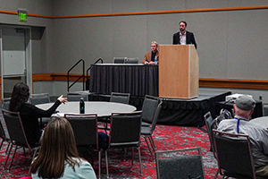 Two presenters speaking in front of an audience.