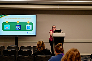 Speaker presenting to an audience in a conference room, with a slide shown on a screen