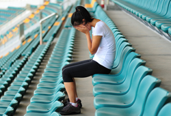 Female student cries into her hands while sitting in an empty row of stadium seats.