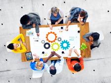 Aerial photo of a group sitting around a table while working on a large paper with colorful gears on it.