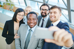 Diverse group of young professionals pose for a group selfie together.