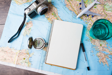Map with a camera, compass, notepad and pen, glass, and model airplane scattered on top of the map.