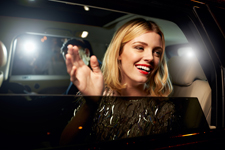 Smiling female waves out the window of a car.