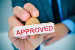 Hand holding a stamp that says "approved" in red lettering.