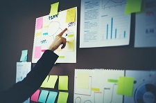 Hand pointing to one piece paper of many pinned to a cork board.
