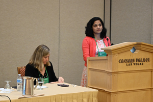 two females, one standing at a podium with "Caesars Palace" visible while the other sits