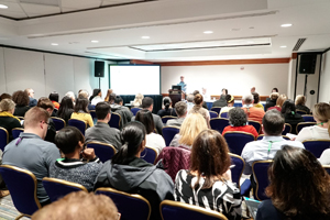 event space full of people listening to a person present from a podium at the front of the room