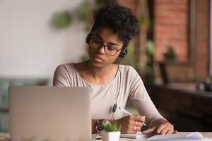 Student in headphones with pen in hand looking at laptop