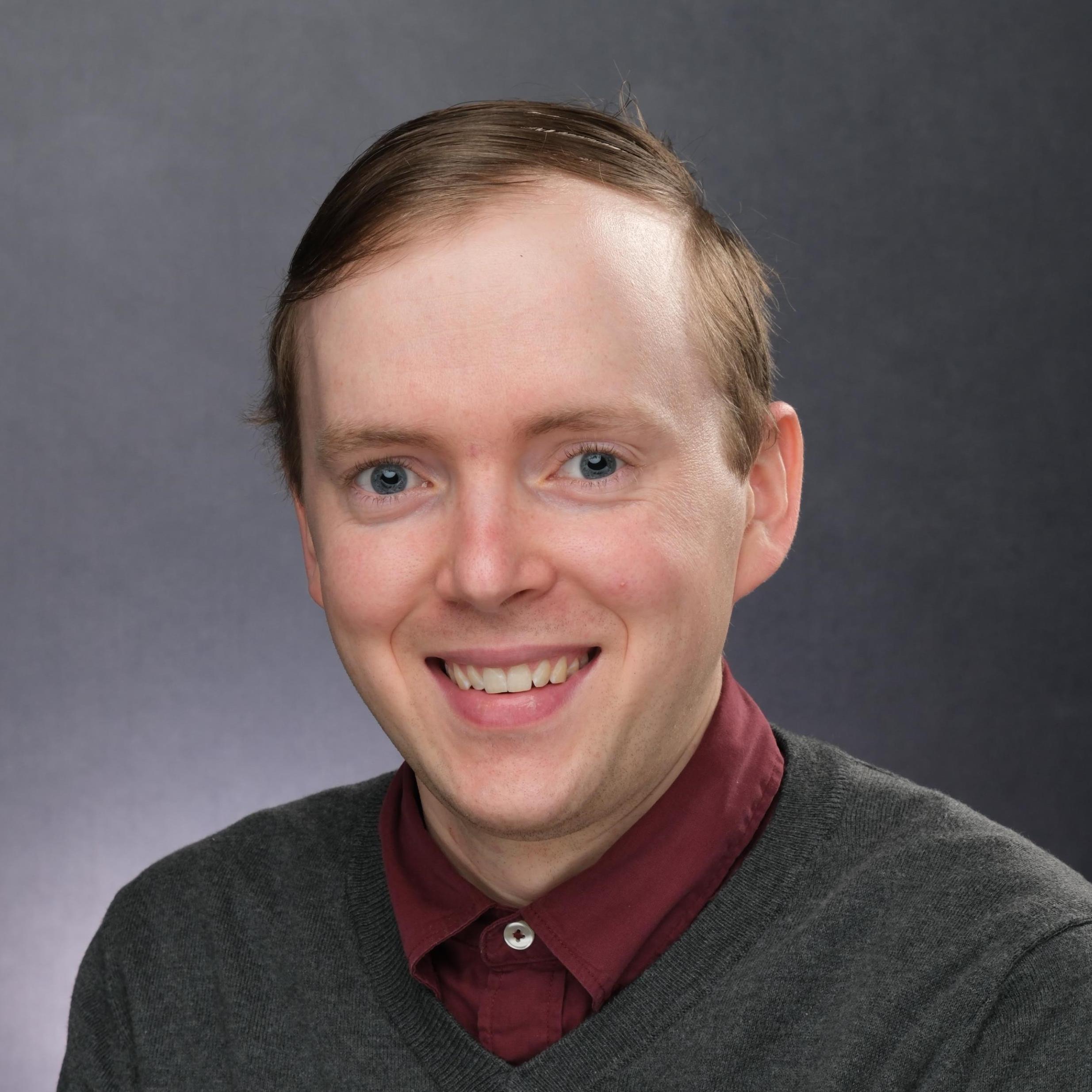 Smiling headshot of a man against a gray background