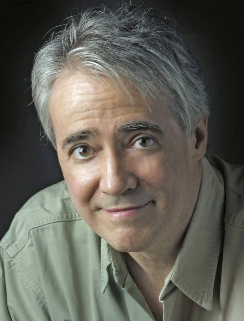 Portrait of an older man with gray hair wearing a light green shirt against a dark background