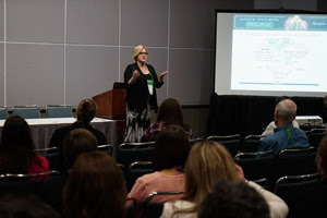 female presenter gesturing with her hands at the front of a room