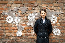 Female standing in front of a red brick wall with a world map displayed on it.