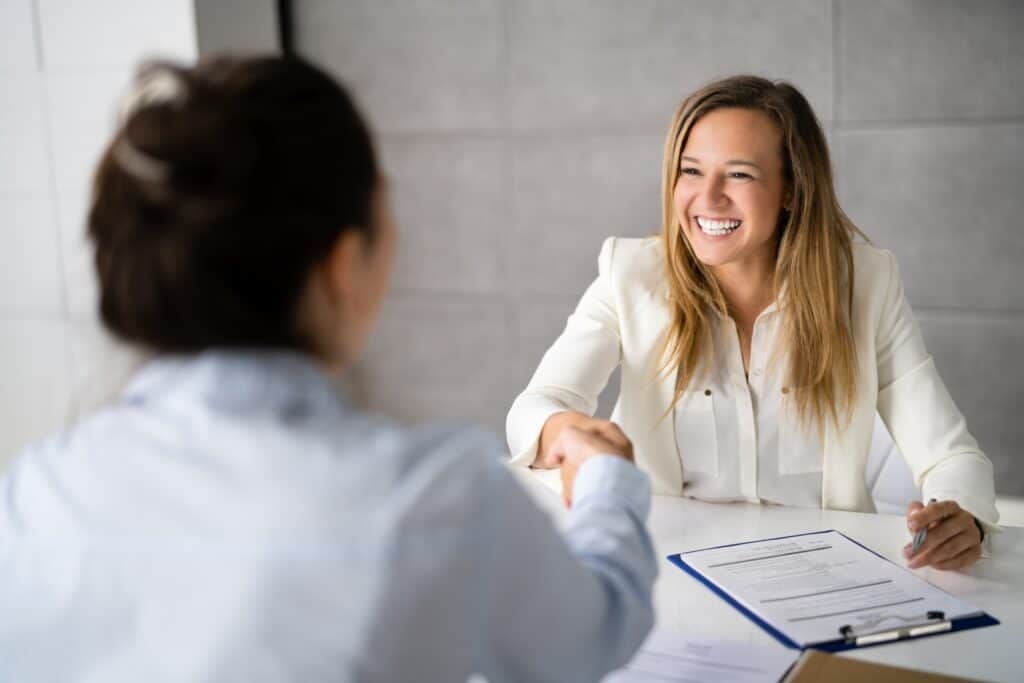 two women shaking hands and smiling in a professional environment