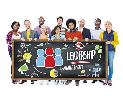 Diverse group of people standing behind a blackboard that says "leadership management" and has various icons drawn in colorful chalk.