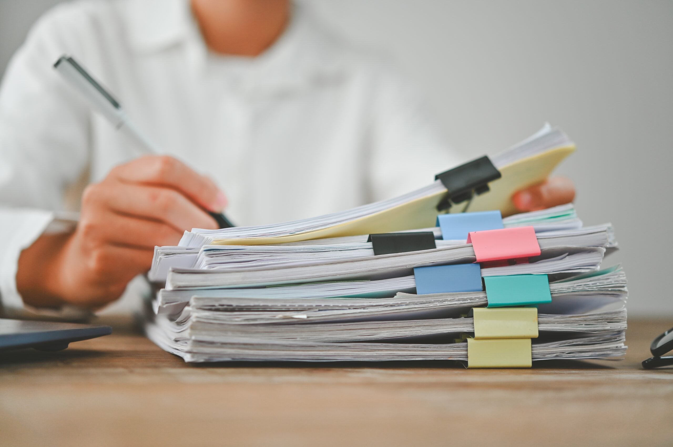 Stack of paper documents marked and clipped in front of a person holding a pen