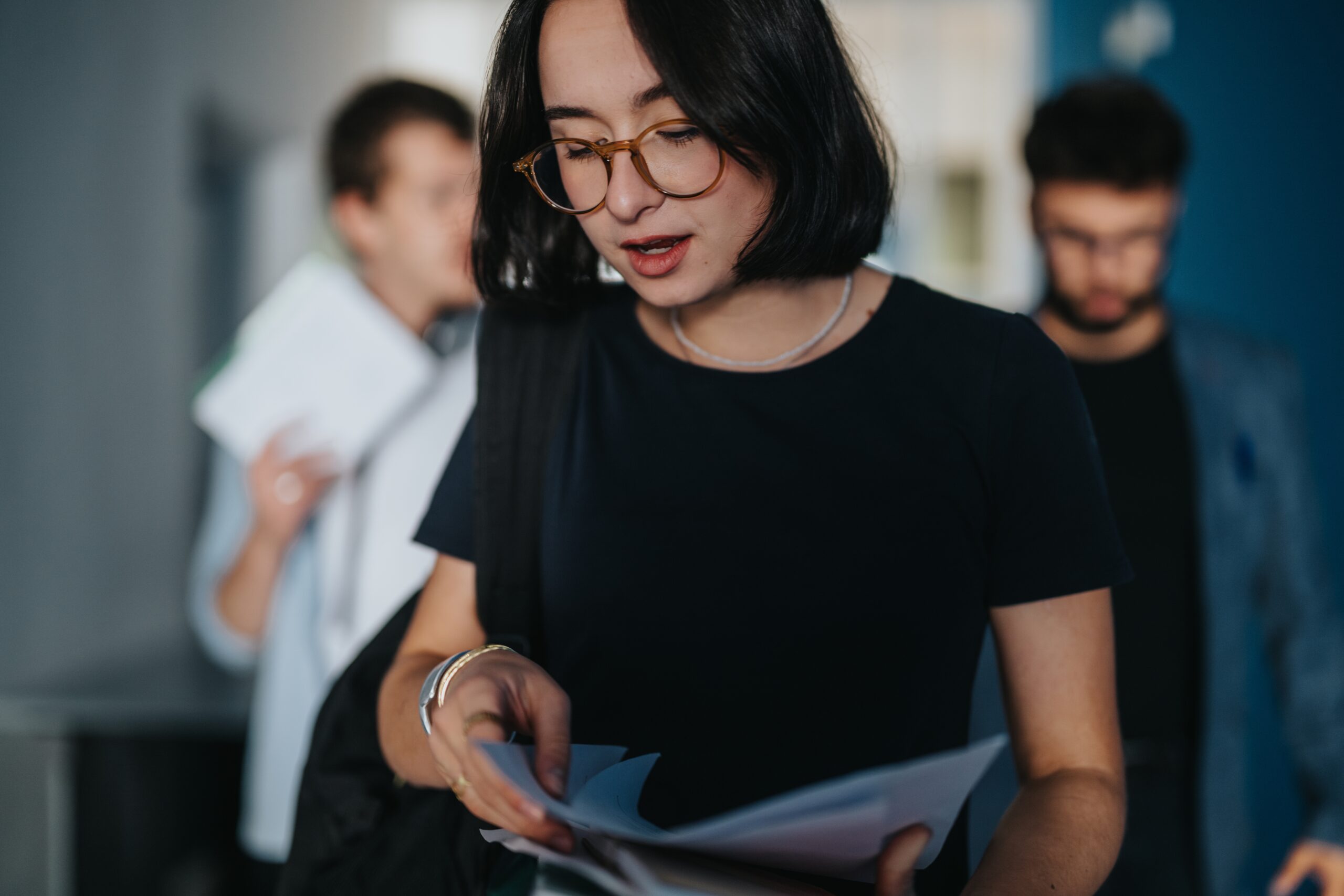 Woman with glasses reading documents while others stand behind her in an office setting
