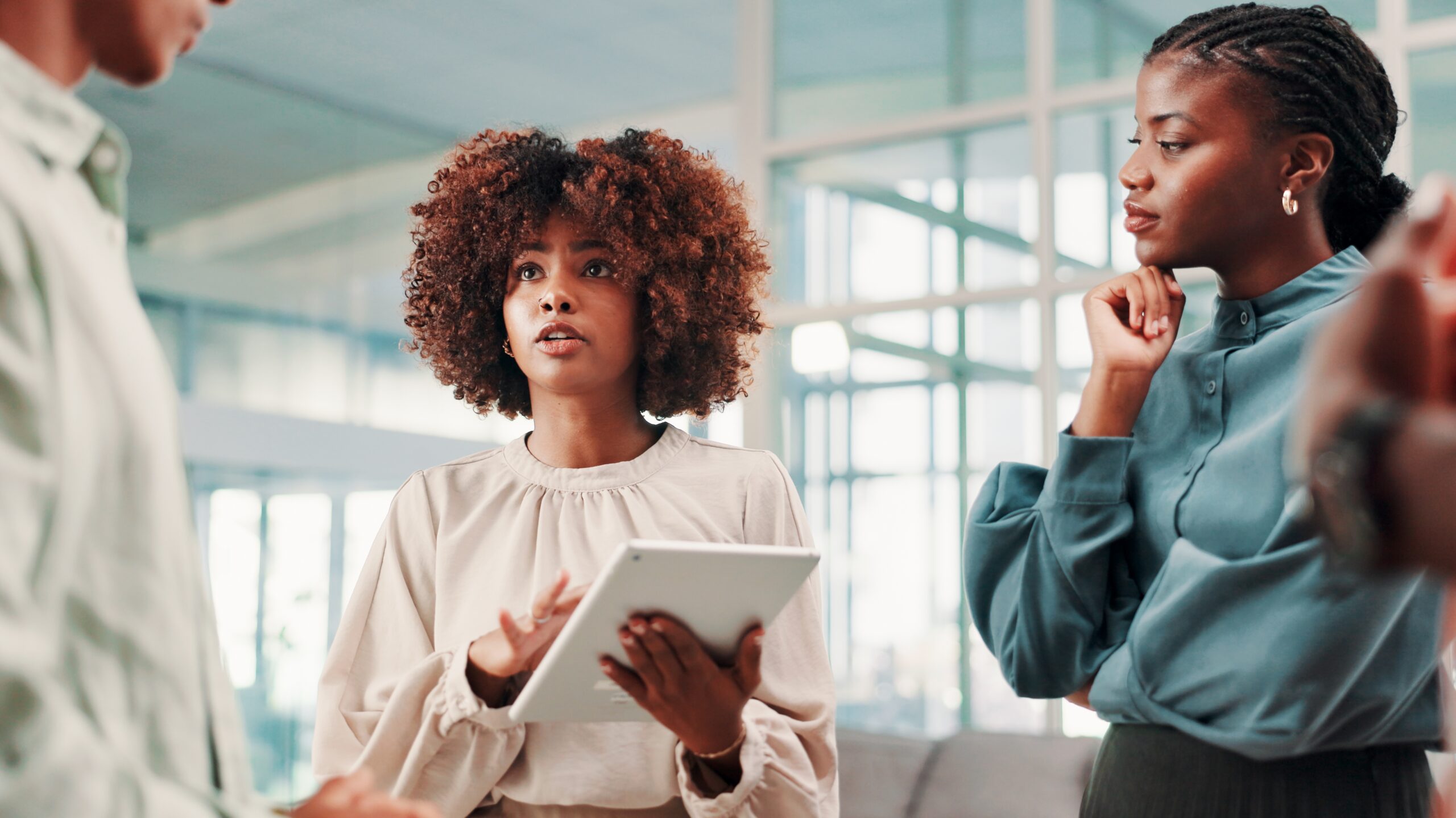 A woman holding a tablet speaks to colleagues in an office setting.A woman holding a tablet speaks to colleagues in an office setting.