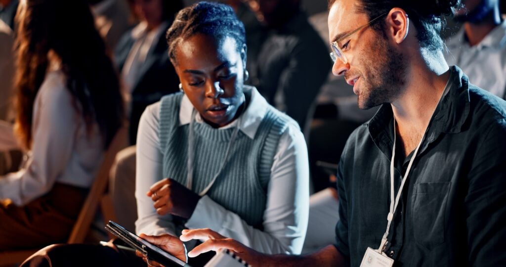 Two conference attendees looking at a device together in a darkened venue.