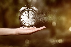Hand holding an analog alarm clock as it dissolves into dust.