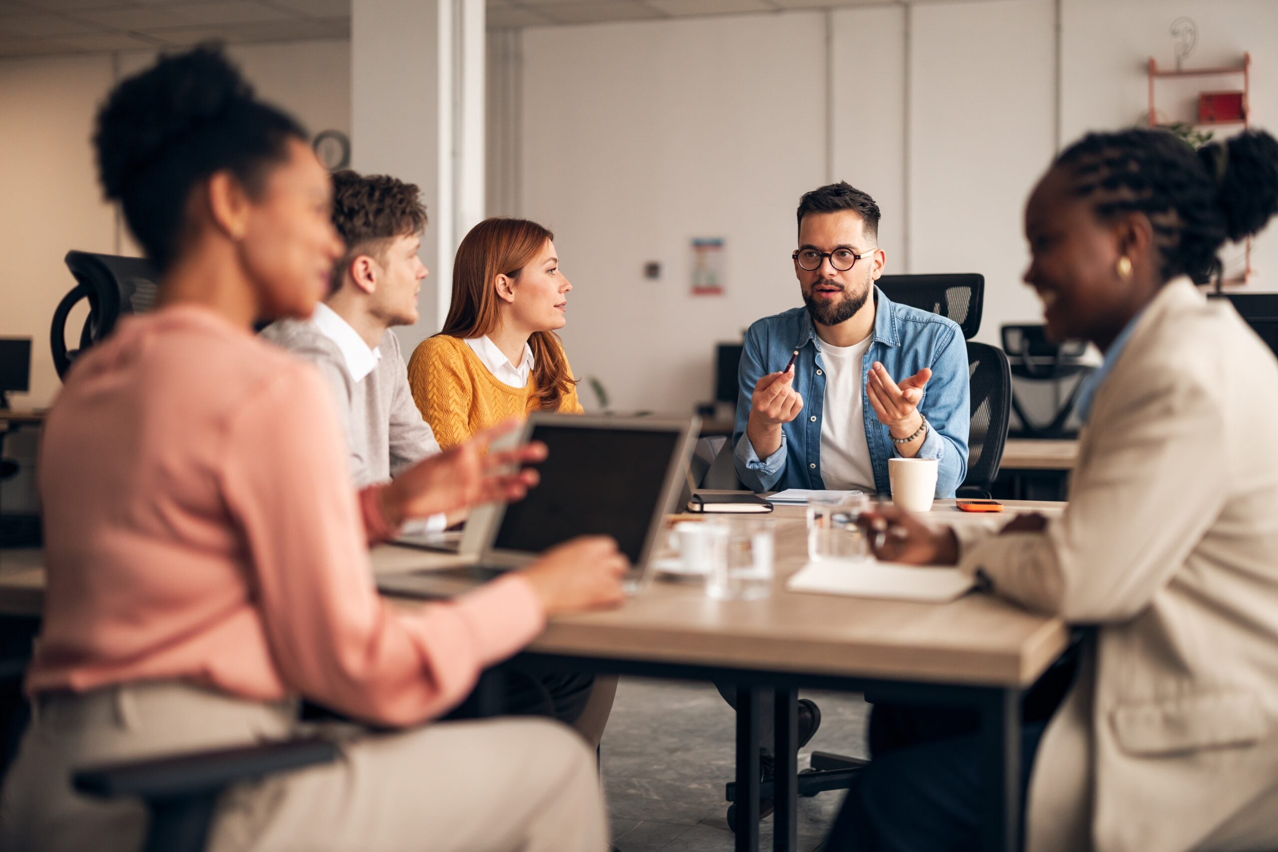 Team meeting in an office, with a man speaking while others listen around a table