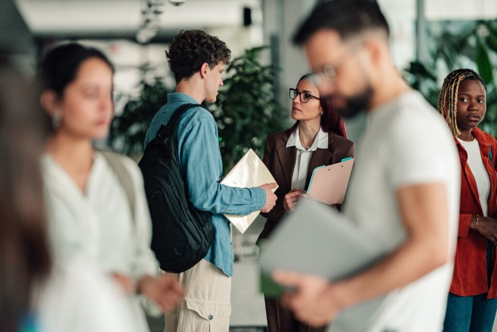 A professor speaking with a student in a busy university hallway.