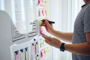 person writing on a whiteboard with many post-its stuck to the surface