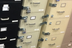 Metal filing drawers with multiple small labels and handles in an office storage area