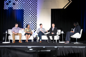 four panelists sit on a couch on a stage with a moderator off to the right side