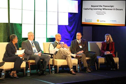 Panel of five people sitting in cushioned chairs, presumably on a stage.