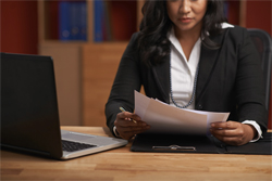Female of color looking at assorted documents with her laptop open next to her.