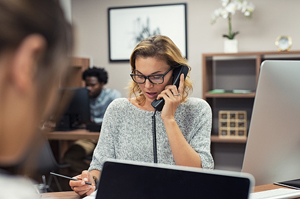 Young professional female on phone taking notes in office.