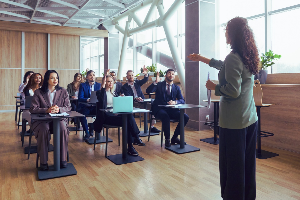 A group of professionals in a classroom; some raising their hands.
