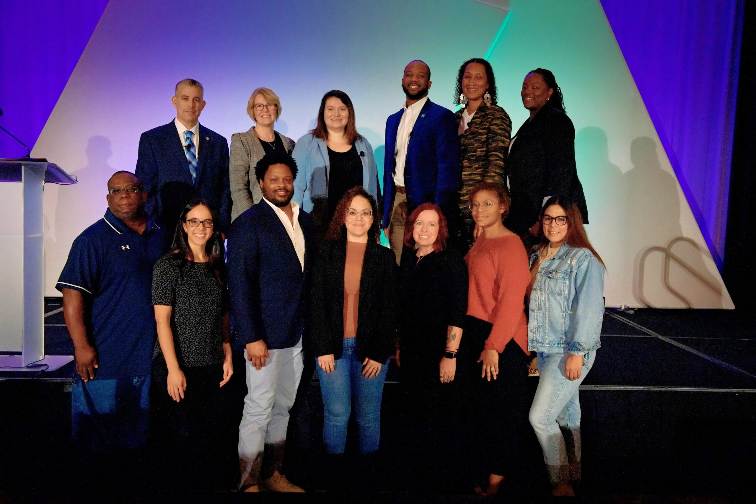 Group of 13 people standing in two rows wearing business casual
